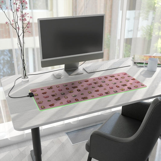 A pink Stardew Valley animals pixel art desk mat with LED lighting sits on a white desk next to a computer monitor and other office supplies.