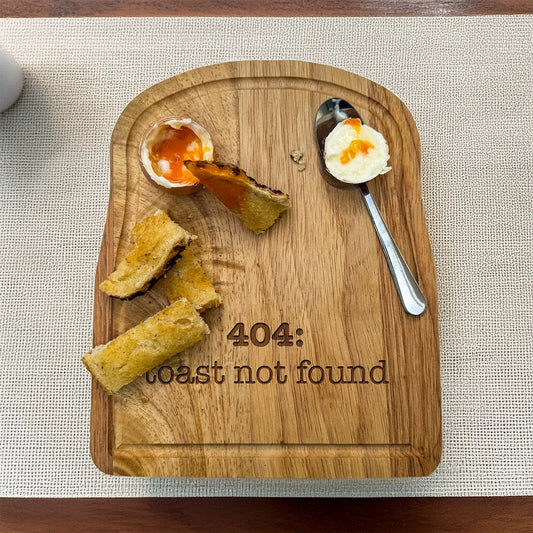 A rubberwood breakfast board featuring the text 404: Toast Not Found, accompanied by a soft-boiled egg and pieces of toast soldiers.