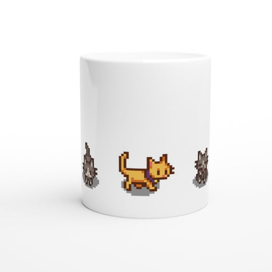 A white mug displays pixelated graphics of ginger and tabby cats, referencing characters from the Stardew Valley computer game.