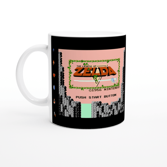 A white mug displays a reproduction of the 1986 Nintendo NES title screen for The Legend of Zelda, featuring pixelated graphics and the words "PUSH START BUTTON.