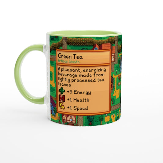 A green ceramic mug features a Stardew Valley-inspired design depicting a Green Tea Artisan Goods label and pixelated landscape around its perimeter, accented by a light green handle.