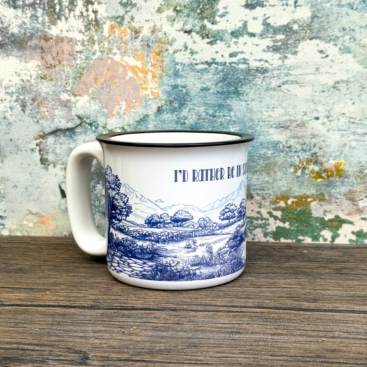 White mug with blue Stardew landscape design and text on a wooden surface with a textured background