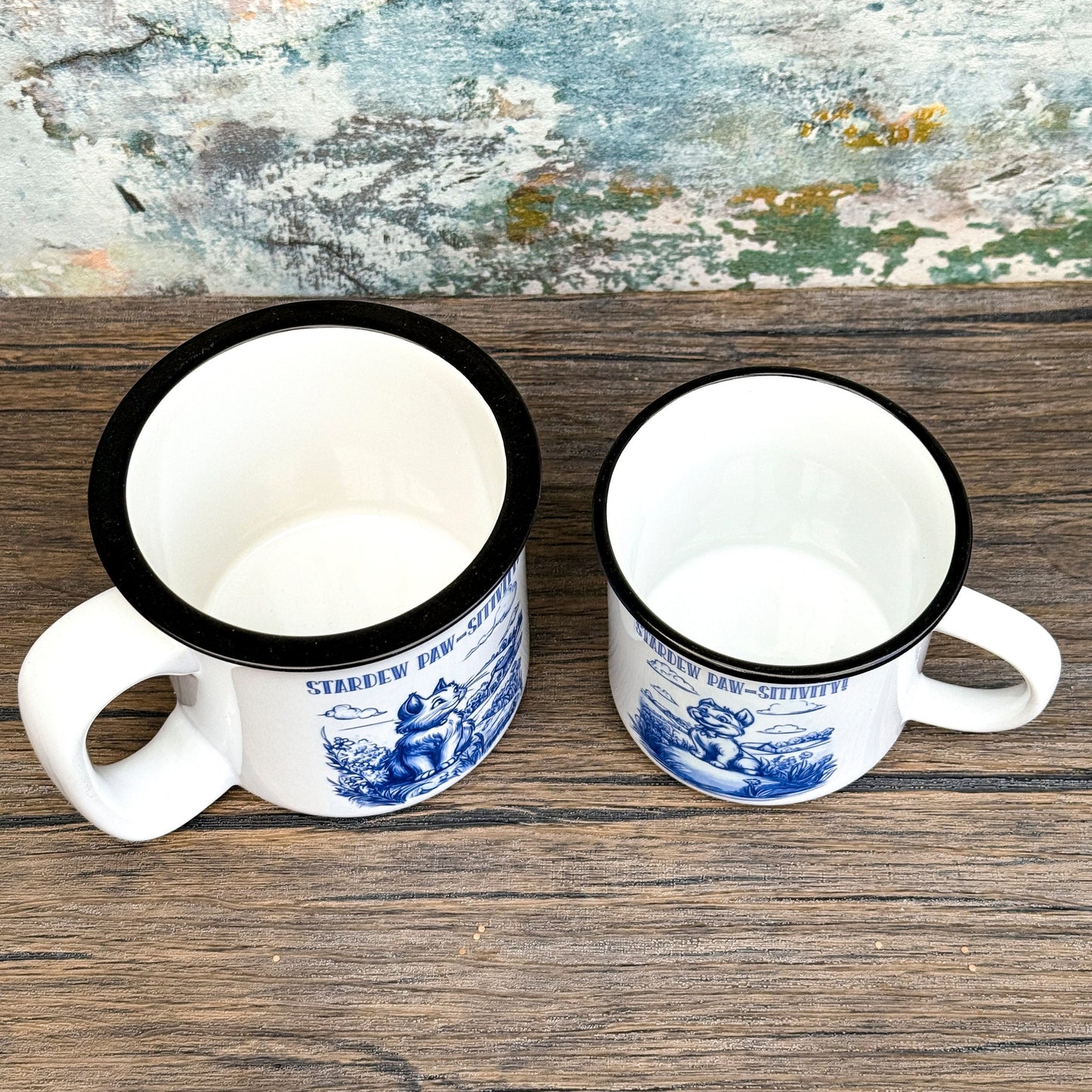 The Quirkify Stardew Valley Chinoiserie Campfire Mug is a blue and white toile ceramic cup featuring house, tree, and mountain artwork with "Stardew Valley" printed on it, displayed on a wooden surface against a multicolored wall.