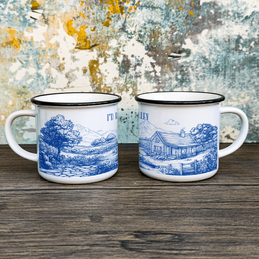 Two enamel camping cups feature a blue and white Stardew Valley-inspired toile de Jouy design depicting landscapes and buildings.