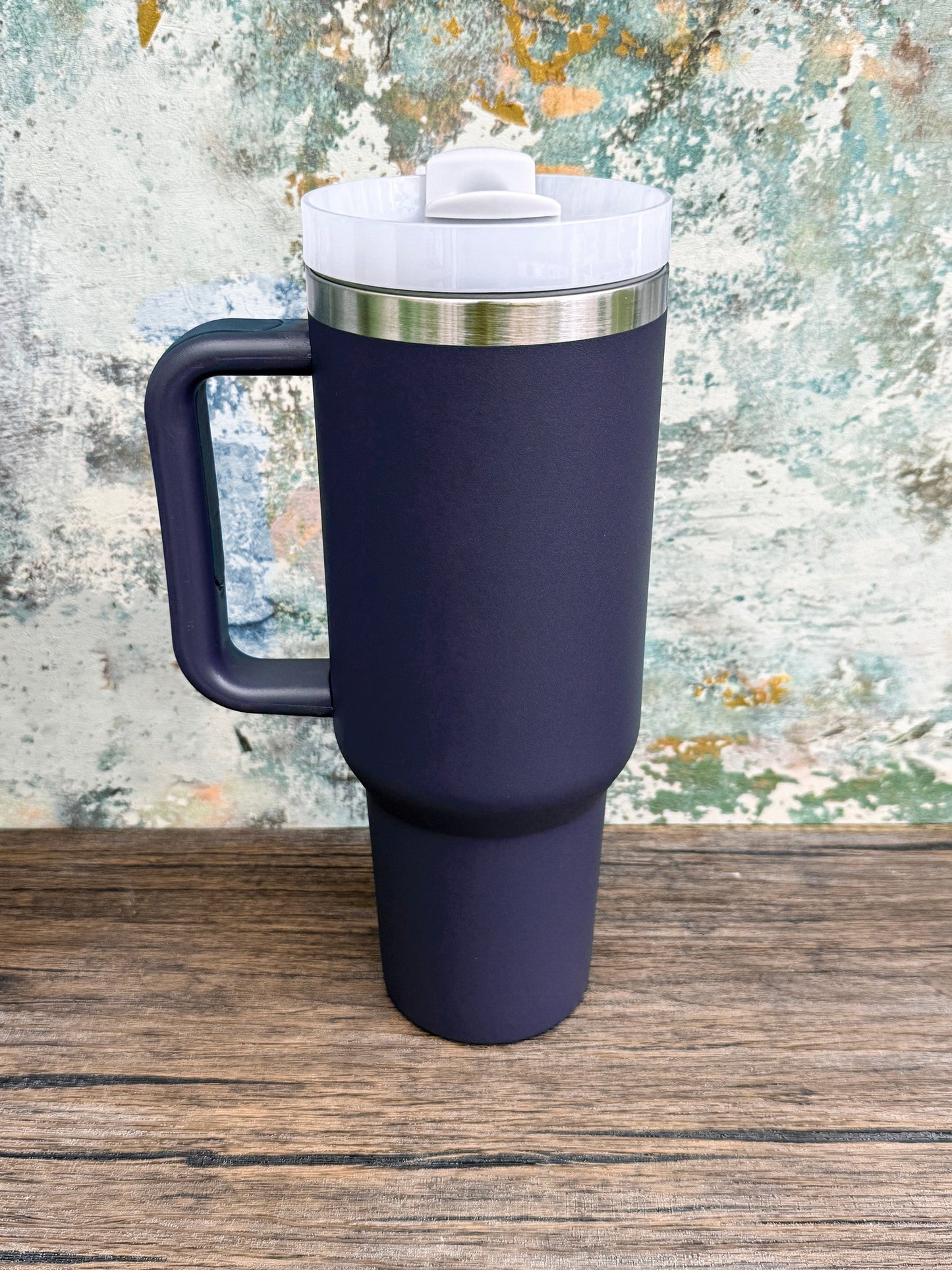 A dark blue 40oz tumbler with a handle and lid sits on a wooden surface.