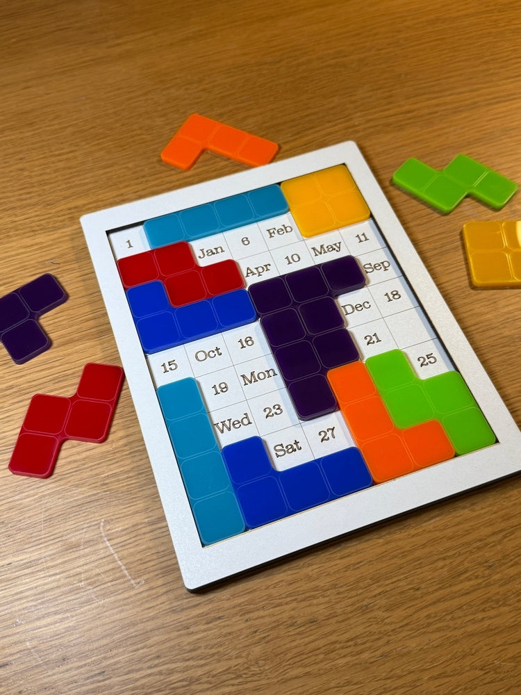 A white desk calendar featuring colorful falling block pieces arranged over dates and months in a retro block puzzle style.