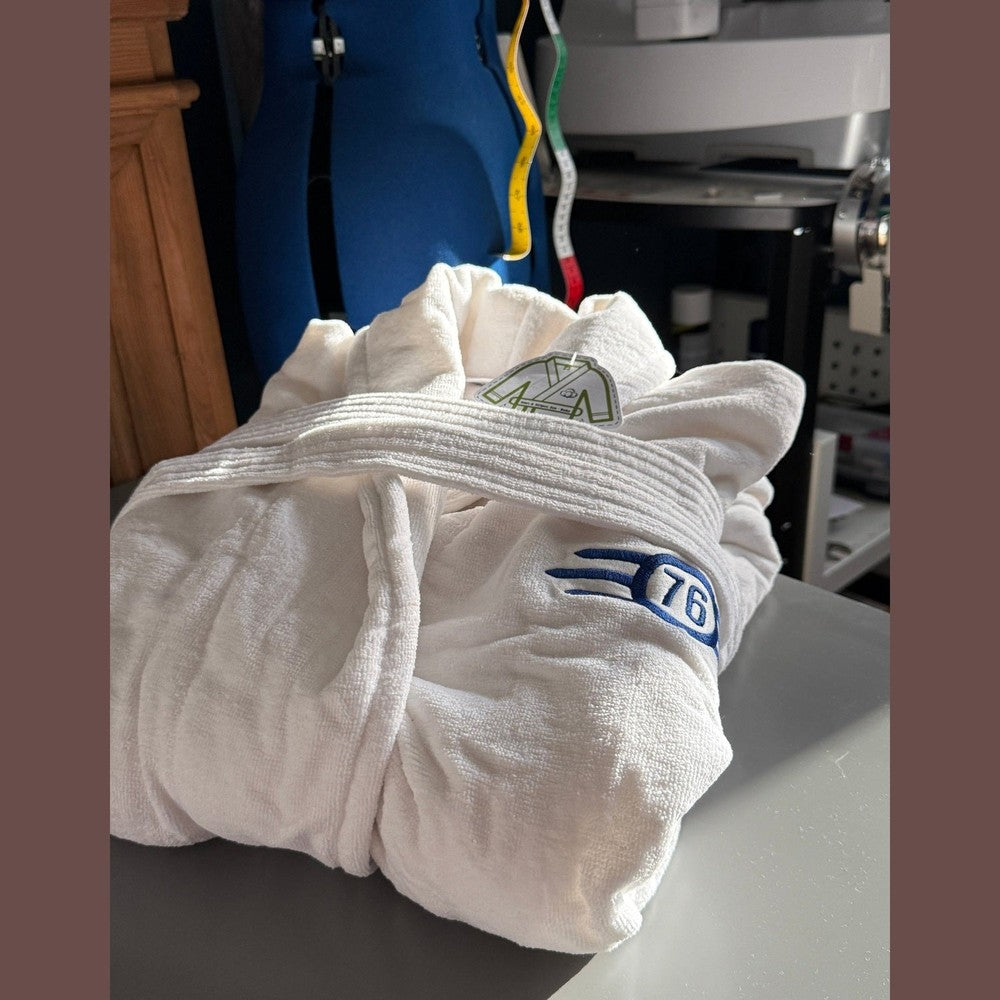 A folded white bathrobe featuring the blue and yellow Fallout Vault-Tec logo and number 76.