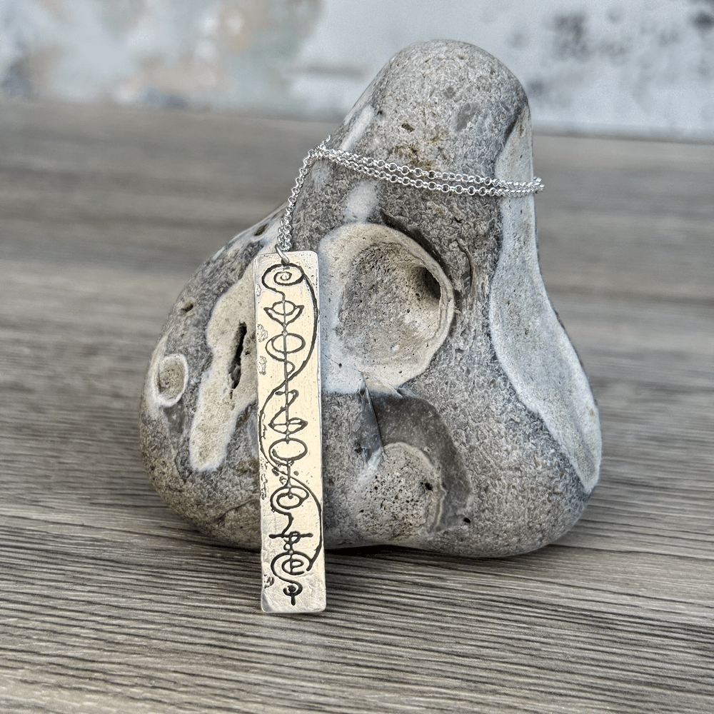 A sterling silver Vulcan IDIC pendant necklace features calligraphy etching on a rectangular charm suspended from a delicate chain.
