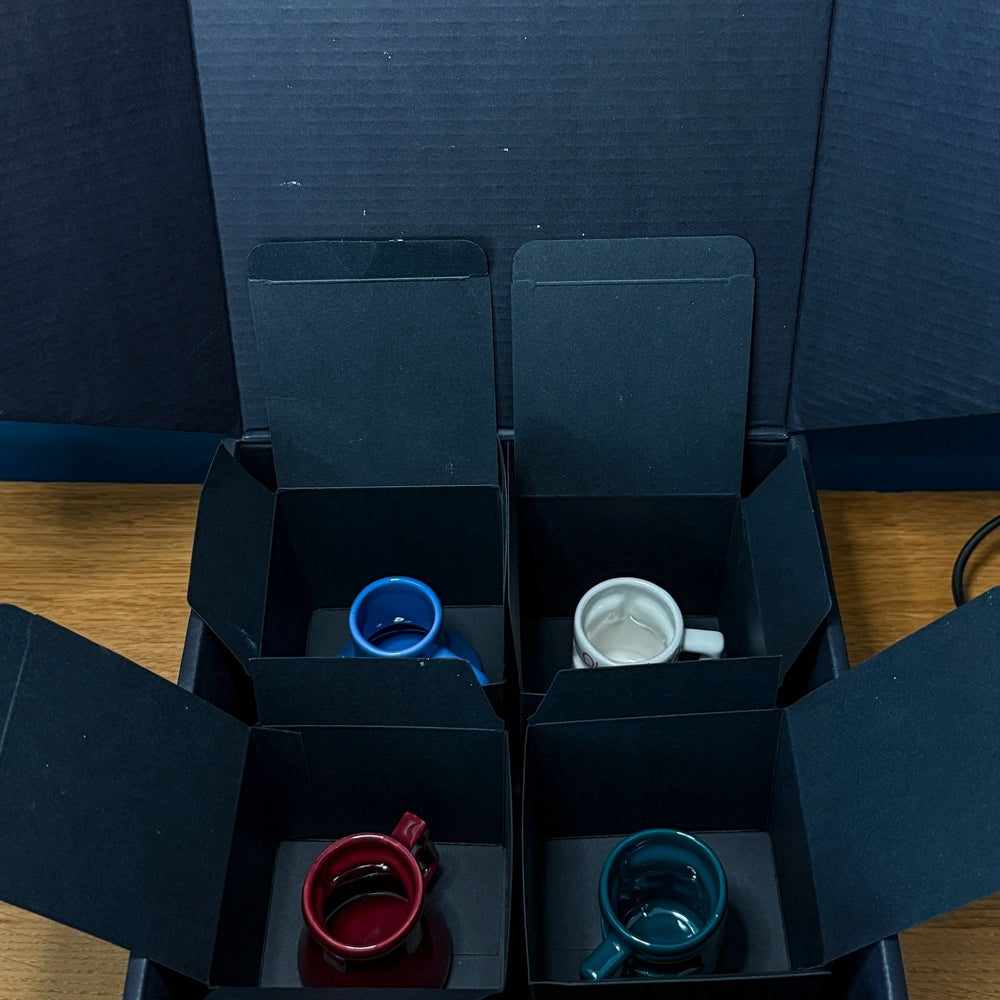 Four small colorful mugs for espresso or shots are displayed inside individual black compartments of a DS9 Mini Raktajino Mug Set box.