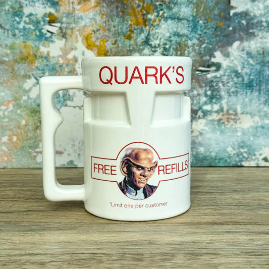 Quarks Bar Mug replica from Star Trek Deep Space Nine labelled "Quark's" with a portrait of Quark and text promoting free refills, against a colourful background