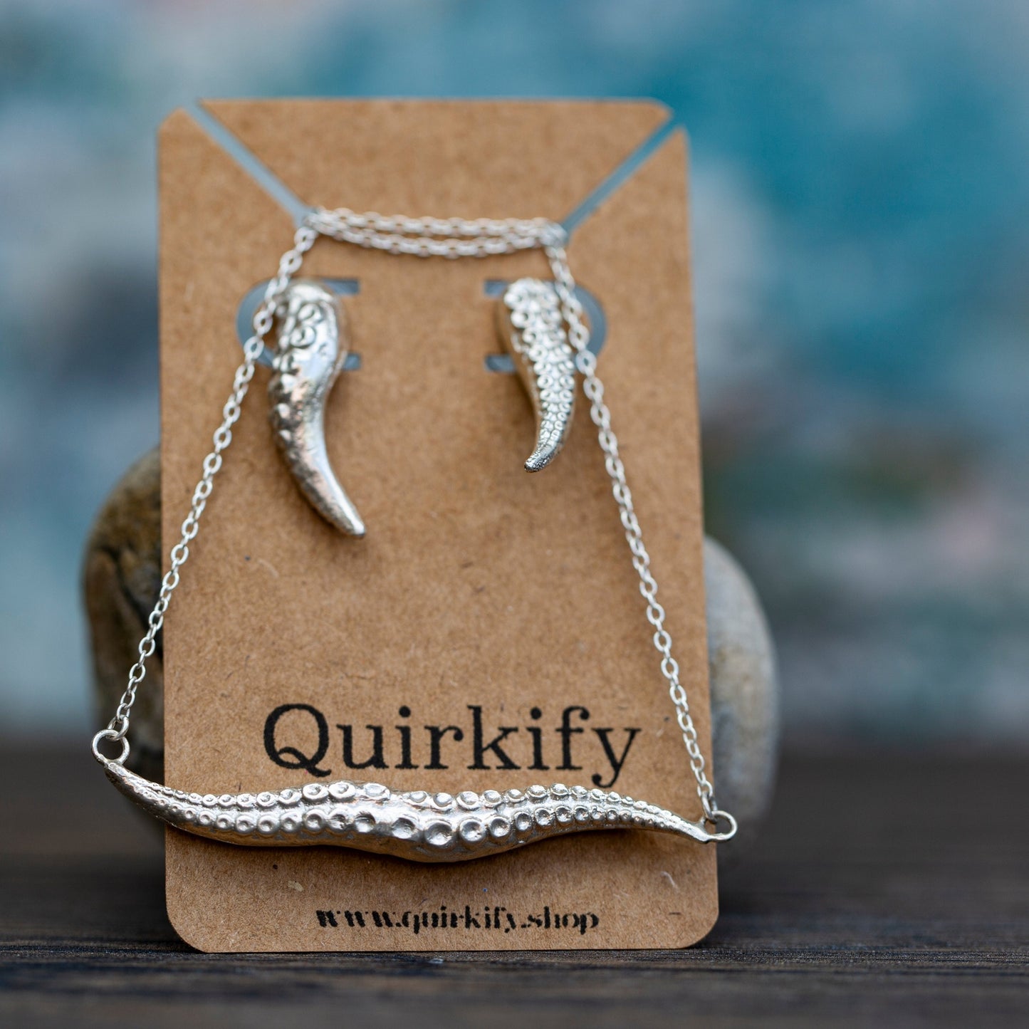 Silver necklace and earrings on a Quirkify branded card with a blurred background