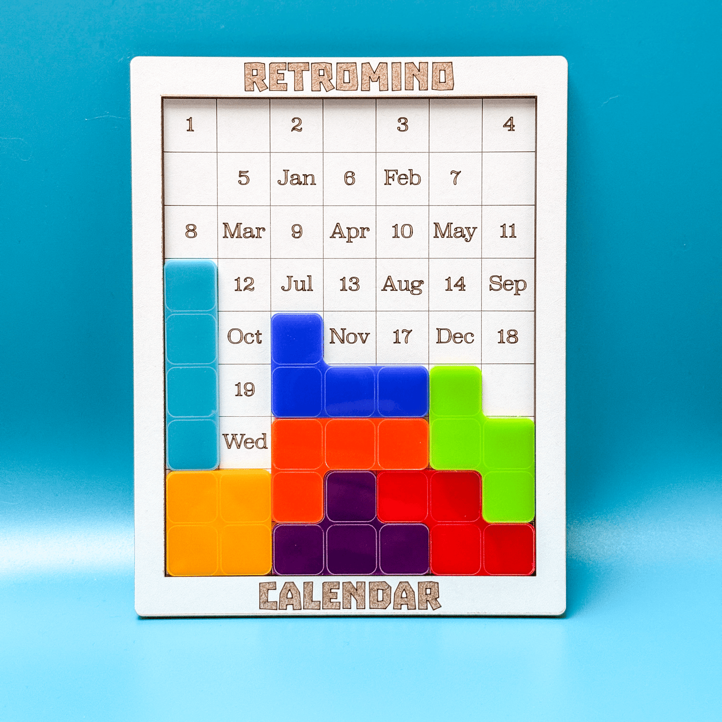 A white KronoBlox puzzle calendar displays dates arranged as Tetromino shapes and labeled with months and days of the week.