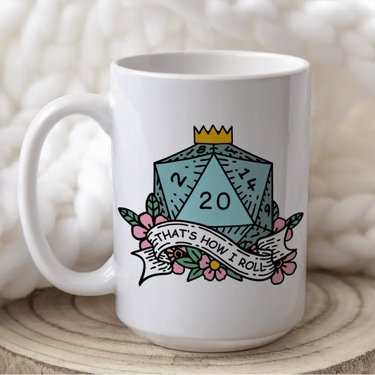 A white mug displays a D&D-themed design featuring a blue twenty-sided die (d20) surrounded by flowers and the phrase "That's How I Roll".