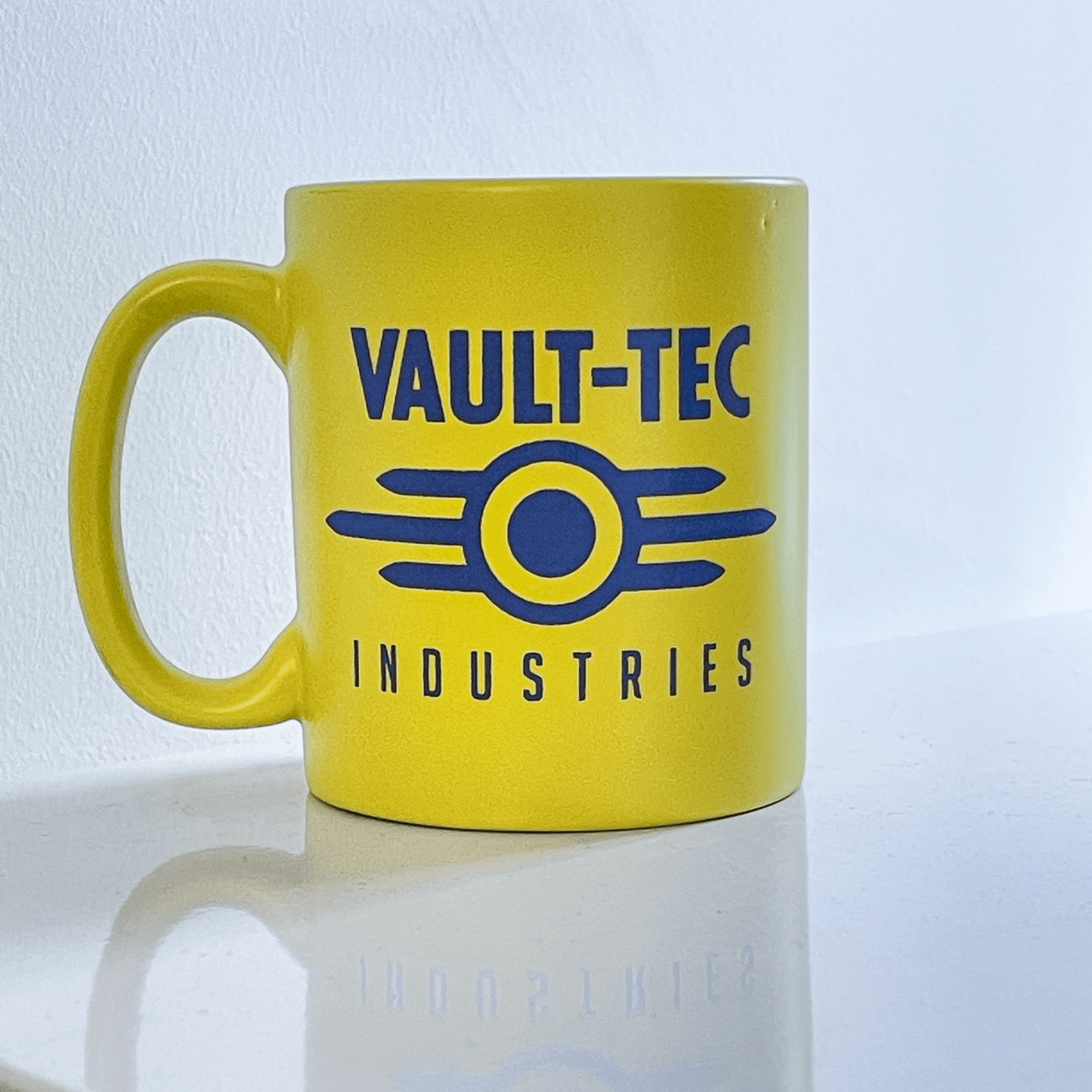 A yellow Fallout mug displays the Vault-Tec Industries logo in blue.