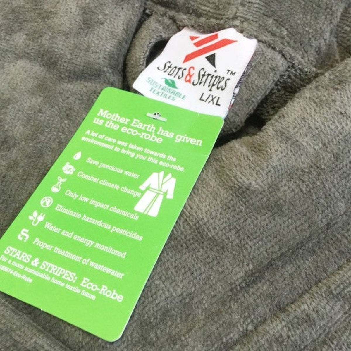 A green tag attached to a gray bathrobe details sustainable textile practices and lists size L/XL under the Stars & Stripes brand name.