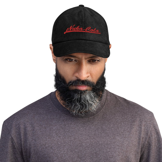 A man wearing a black Nuka Cola embroidered dad hat looks directly at the camera.