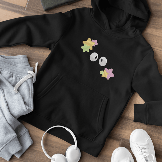 A black Soot Sprites embroidered hoodie, inspired by Studio Ghibli, is laid out on a wooden surface with matching sweatpants and sneakers.