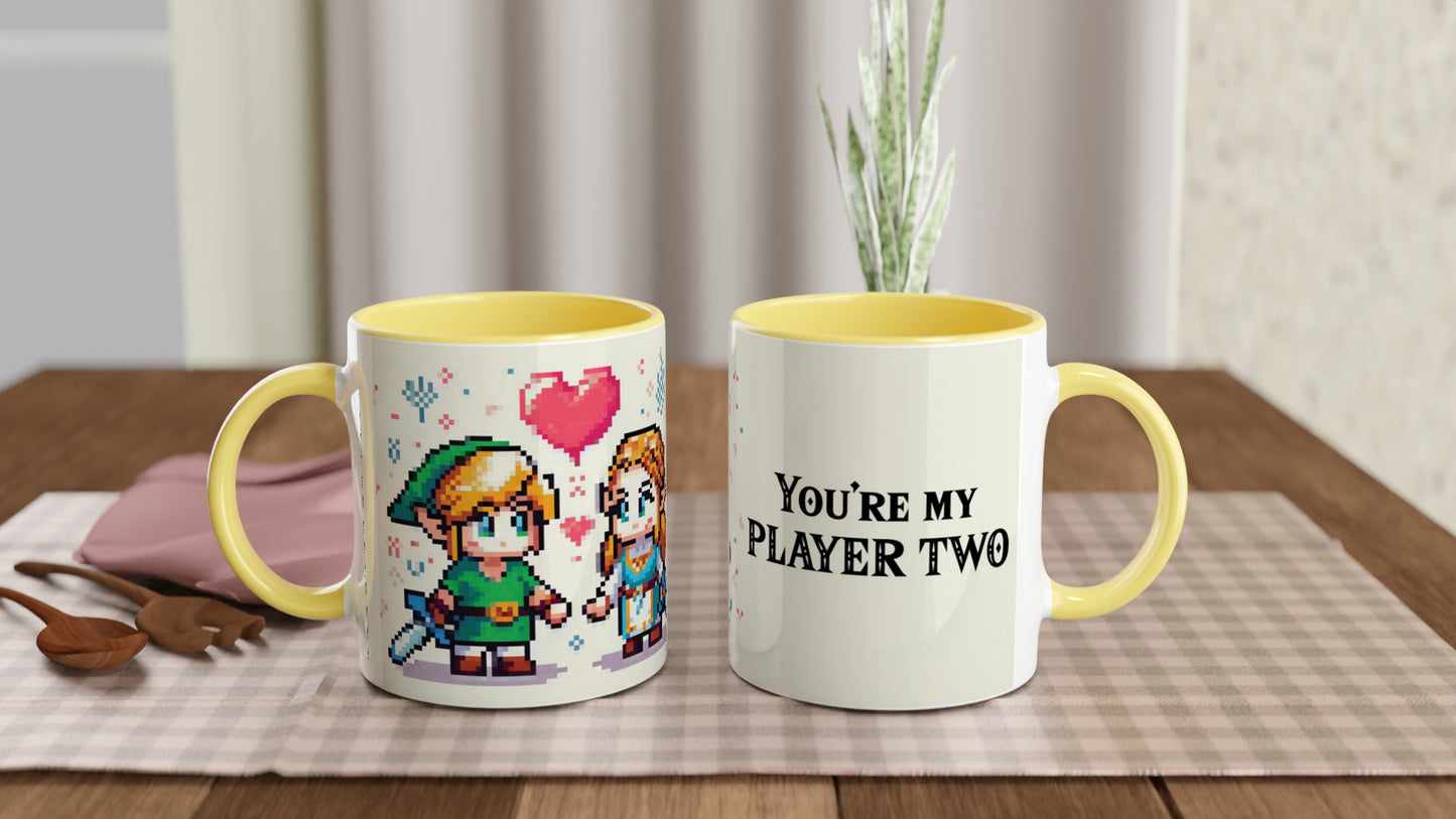 A white mug with a yellow handle features pixel art of Link and Zelda from The Legend of Zelda, along with the text "You're My Player Two.