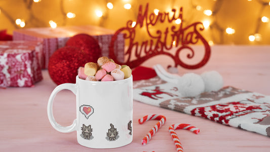 A white mug with Stardew Valley Cats on, in a Christmas setting with fairy lights and candy canes