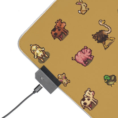 A rectangular desk mat features pixel art depictions of Stardew Valley animals on a yellow background and includes a connected USB cable for its LED lighting.