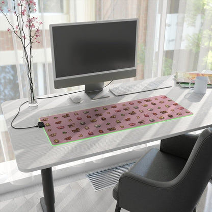 A pink Stardew Valley animals pixel art desk mat with LED lighting sits on a white desk next to a computer monitor and other office supplies.