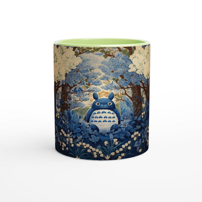 A ceramic mug depicts Totoro from Studio Ghibli sitting within a blue and white cherry blossom forest scene in a chinoiserie style.