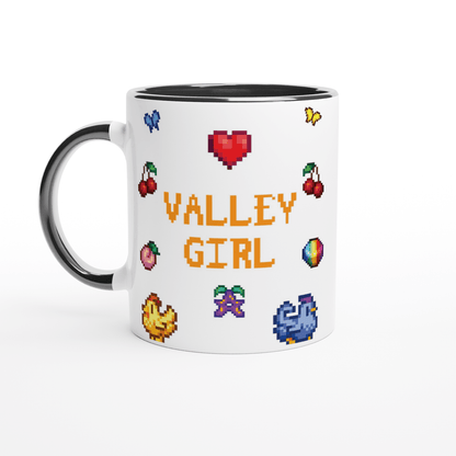A white coffee mug with a black handle and rim features pixel art icons from Stardew Valley including cherries, chickens, a prismatic stardrop, and the words "Valley Girl.