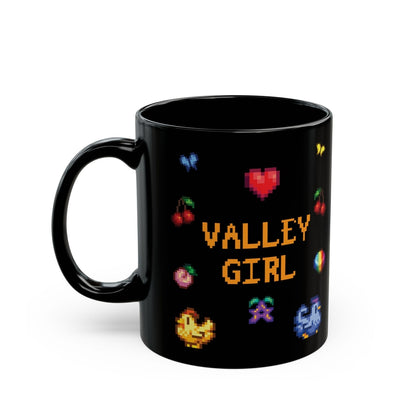 A black coffee mug displays pixel art sprites / graphics from Stardew Valley including a heart, cherries, a prismatic shard, a stardrop, and butterflies.