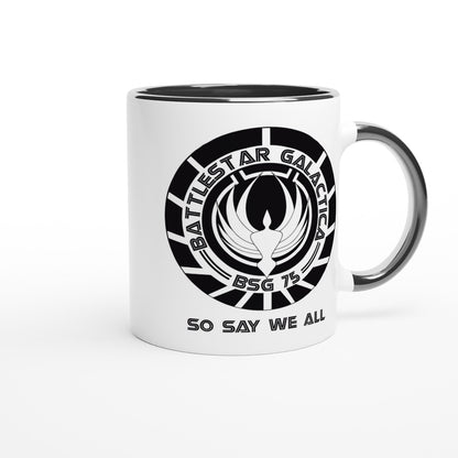 A white ceramic mug features a black rim and handle, displaying the Battlestar Galactica logo with "BSG 75" and "So Say We All" printed around it.