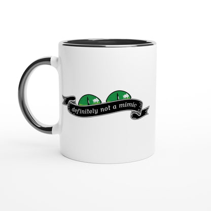 A white mug with a black handle and rim features a graphic of green eyes and a banner reading "definitely not a mimic," referencing the D&D tabletop RPG game.