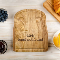 A rubberwood breakfast board featuring the engraved text 404: toast not found is shown on a white wooden surface alongside blueberries, jam, and orange juice.