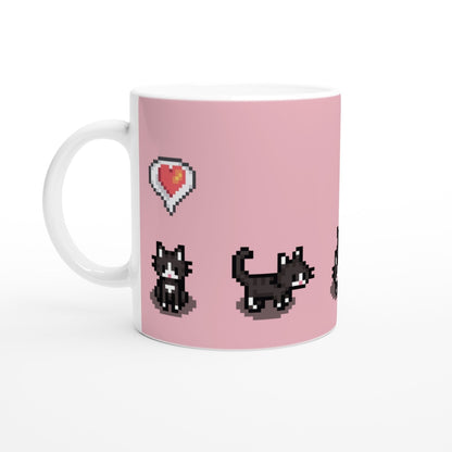 A white mug displays pixelated graphics from Stardew Valley featuring tuxedo cats and a heart emote on a pink background.