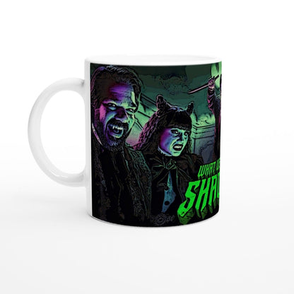 A white mug displays a stylized illustration of Laszlo and Nadja from What We Do In The Shadows, along with green lettering on the right side.