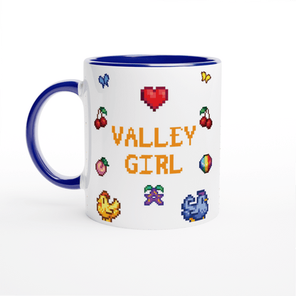A white coffee mug with a blue rim features pixel art icons from Stardew Valley including chickens, cherries, a heart, and the words "Valley Girl.