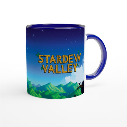 A ceramic tea mug features a blue background depicting a nighttime scene from Stardew Valley with mountains and trees, accented by a matching coloured handle.