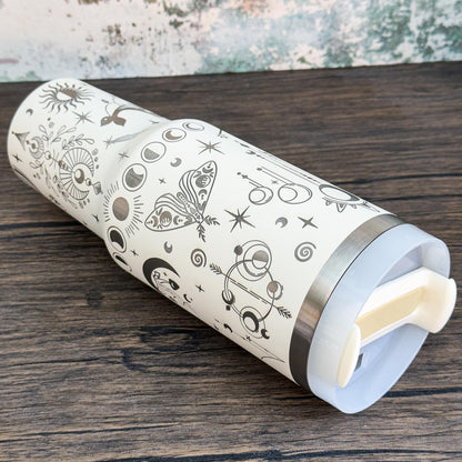A silver tumbler featuring a celestial design of stars, moons, and crystals evokes a witchy boho aesthetic.