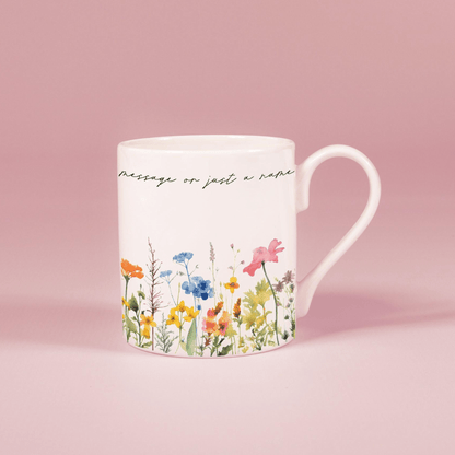 A white china mug features a watercolour floral design of wildflowers along with handwritten script reading "message or just a nap".