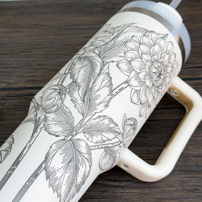 A white 40oz tumbler features a unique engraved botanical design of floral dahlias.