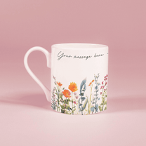 A white china mug features a watercolour floral design of wildflowers along with the text "Your message here".