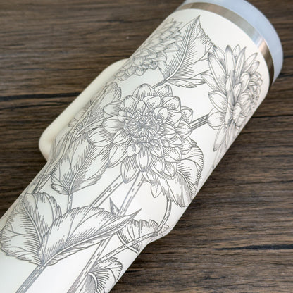 A close-up shows a white Floral Dahlias 40oz Tumbler featuring an engraved botanical design of dahlia flowers and leaves.