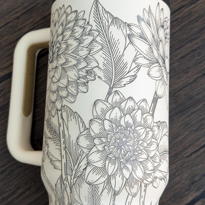 A white 40oz tumbler features a detailed engraved botanical design of floral dahlias.