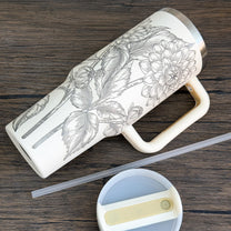 A cream-colored 40oz tumbler features a unique engraved botanical design of floral dahlias.
