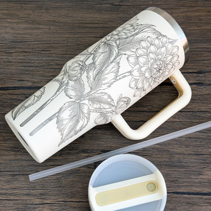 A cream-colored 40oz tumbler features a unique engraved botanical design of floral dahlias.
