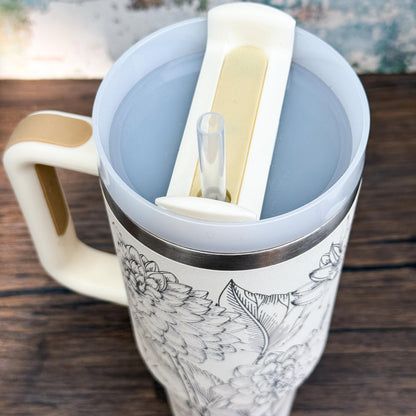 A close-up shows a Floral Dahlias 40oz Tumbler with an engraved botanical design and its lid partially open revealing a drinking spout.
