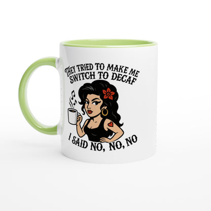 A white coffee mug with a green handle and rim features an illustration of Amy Winehouse holding a cup and text referencing "no to decaf.