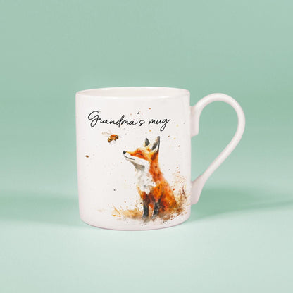 A white china mug features a watercolour illustration of a fox alongside a bee, and includes the handwritten phrase "Grandma's mug".