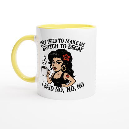 A white coffee mug with a yellow handle and rim features an illustration of Amy Winehouse holding a cup and text referencing "no to decaf.