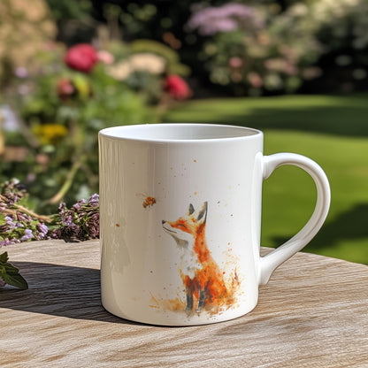 A white china mug displays a watercolour illustration of a fox and bee.