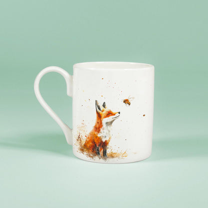 A white china mug displays a watercolour illustration of a fox and a bee.