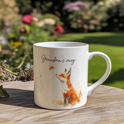 A white china mug features a watercolour illustration of a fox alongside a bee, and is inscribed with "Grandma's mug".